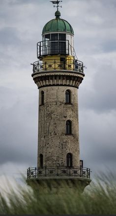 a tall light house sitting on top of a lush green field under a cloudy sky