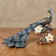 a peacock figurine sitting on top of a wooden table next to a white flower