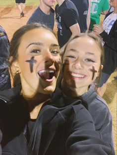 two girls with face paint on their faces posing for the camera at a baseball game