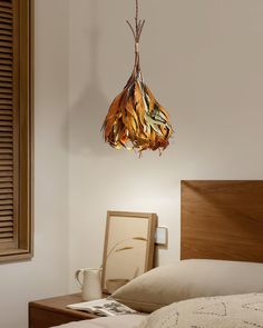 a lamp hanging from the side of a bed next to a night stand and coffee cup