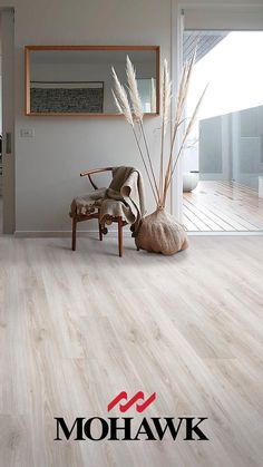 a living room with white wood floors and a chair next to a mirror on the wall