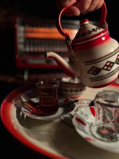 a person pouring tea into a red and white teapot on top of a plate