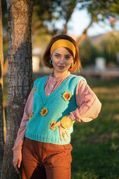 a woman standing next to a tree wearing a blue sweater and yellow headband with sunflowers on it