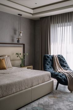 a large bed sitting next to a blue chair in a room with curtains on the windows