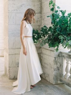 a woman in a white dress standing next to a plant