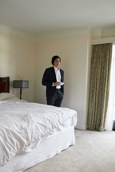 a man in a suit standing next to a bed with white linens on it