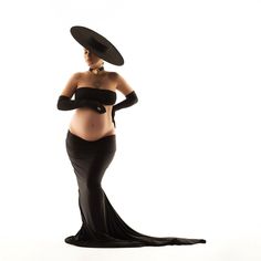 a pregnant woman in a black dress and hat poses for the camera with her hands on her hips