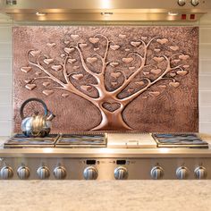 a stove top with a tea kettle on it next to a wall mounted copper tree