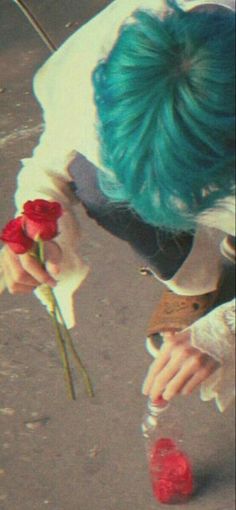 a person with blue hair and green hair is holding flowers in their hands while looking down at the ground