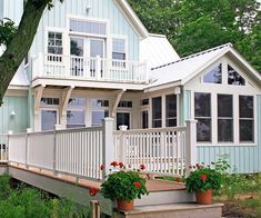 a blue house with white railings and flowers on the front porch, surrounded by greenery