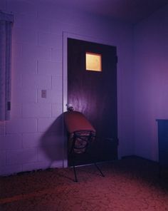 an empty room with a chair in the corner and a purple light coming through the window