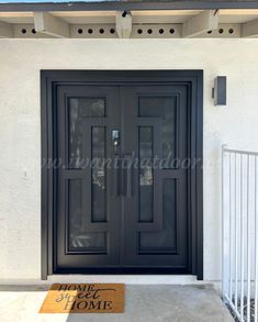 a black front door with two sidelights and a welcome mat on the concrete floor