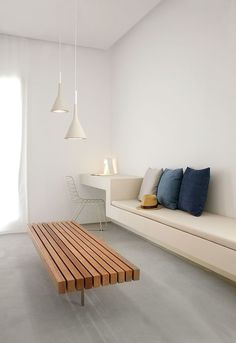 a white room with a wooden bench and table in the corner, next to a window