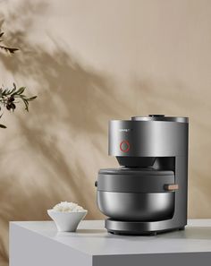 a silver coffee maker sitting on top of a counter next to a bowl of white rice