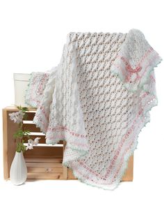 a white crocheted blanket sitting on top of a wooden crate next to a vase