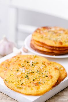 two plates with food on them sitting on a table next to garlic and an onion