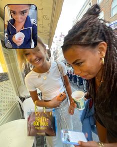 two girls looking at a book together on their cell phone and another girl holding a coffee cup