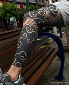 a man is sitting on a bench with his leg covered in black and white tattoos