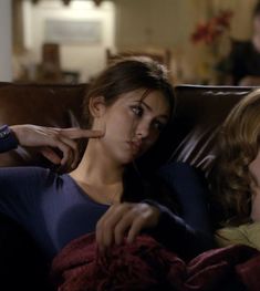 two women sitting on a couch with one pointing at the other woman's finger