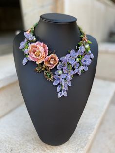 a necklace with flowers on it sitting on a mannequin headpiece in front of a building