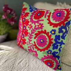 a colorful pillow sitting on top of a bed next to a vase with flowers in it