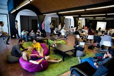 many people are sitting and standing in an open room with bean bags on the floor