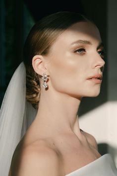 a woman in a white dress and veil with earrings on her head, looking off to the side