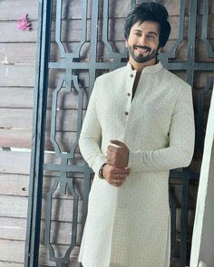 a man standing in front of a wooden wall wearing a white sherve and black pants