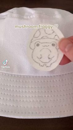 a hand holding a sticker on top of a white hat with a bear drawn on it