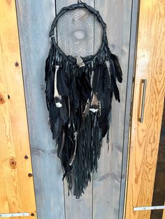 a black dream catcher hanging on the side of a wooden door with feathers attached to it