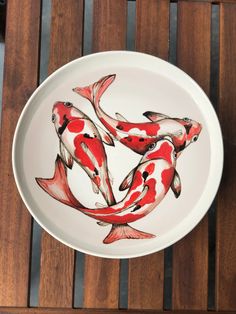 a white plate with red and black koi fish painted on the side sitting on a wooden table