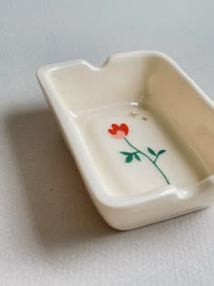 a small white dish with red flowers painted on the front and bottom, sitting on a table