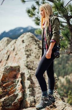 a woman standing on top of a mountain next to a tree and holding a camera