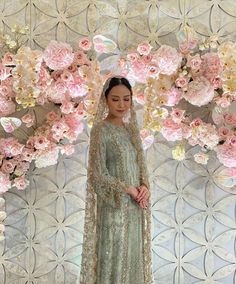 a woman standing in front of flowers wearing a long green dress with gold trims