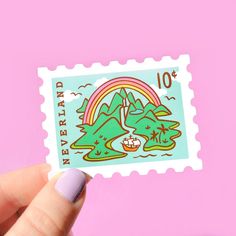 a person holding up a small stamp with an image of a rainbow and mountains on it