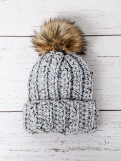 a gray knitted hat with a brown pom - pom sitting on top of it