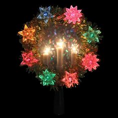 a lighted christmas wreath with candles in the center and stars on it, against a black background