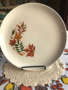 a white plate sitting on top of a doily covered tablecloth with leaves painted on it