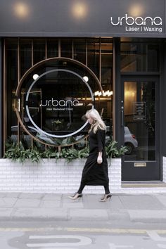 a woman walking down the street in front of a building with a large circular window