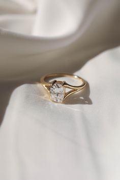 a gold ring with a single diamond on it sitting on a white fabric background,