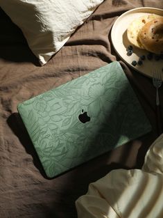 an apple laptop sitting on top of a bed next to a plate with donuts