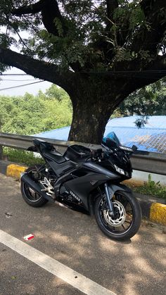 a black motorcycle parked next to a tree on the side of a road in front of a bridge