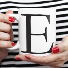 a woman holding a coffee mug with the letter f on it's side and red fingernails