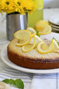 a cake with lemon slices on it sitting on a table next to plates and flowers