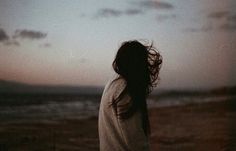 a woman standing on the beach with her hair blowing in the wind at sunset or dawn