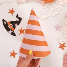 a hand holding a paper party hat on top of a white table with orange and black stars