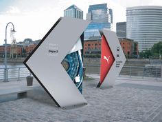 two large white and red signs sitting on top of a brick road next to tall buildings