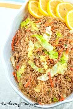 a white bowl filled with noodles and veggies next to sliced lemon wedges