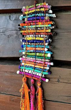 a multicolored wall hanging with tassels and beads on wood planks