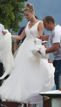 a woman in a white dress is walking down the street with other people around her